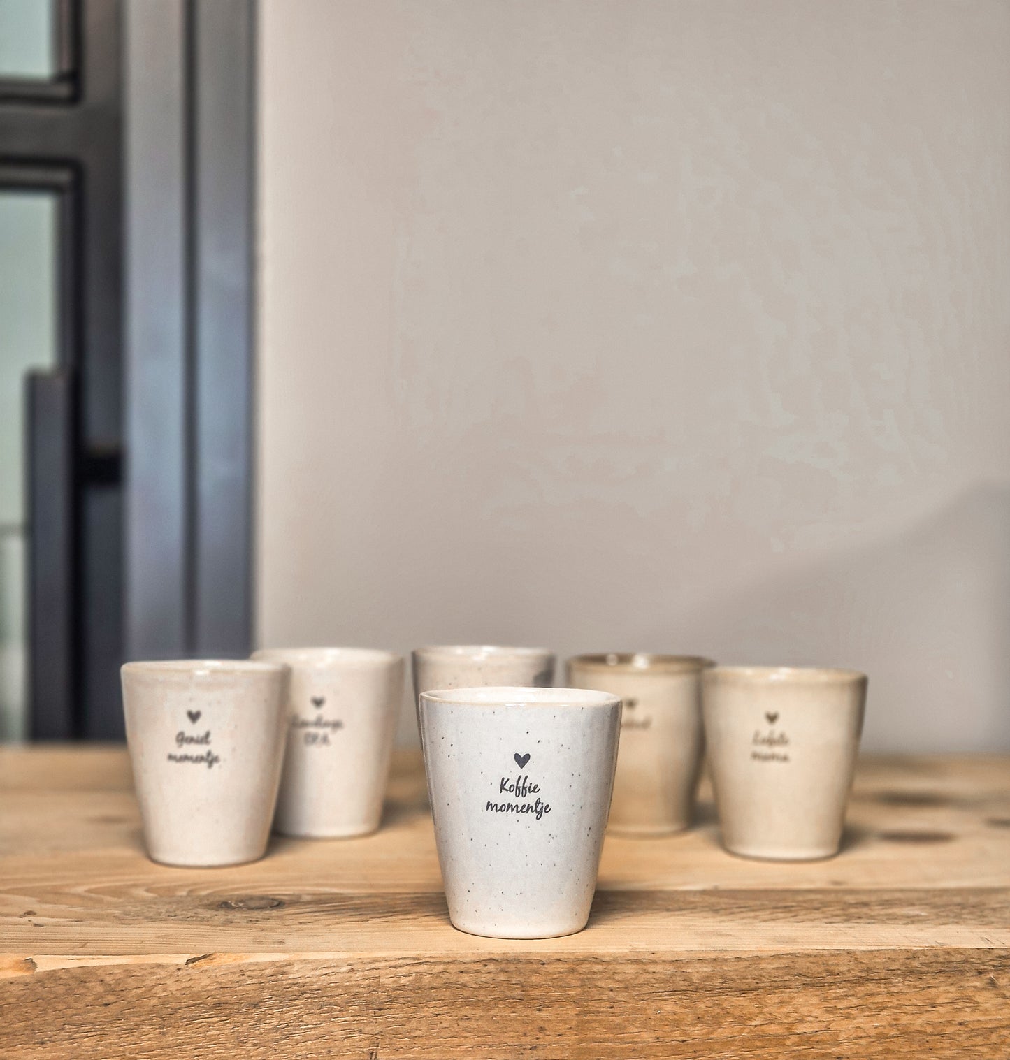 Op de voorgrond mokje met tekst koffiemomentje. Erachter staan nog andere varianten mokjes.