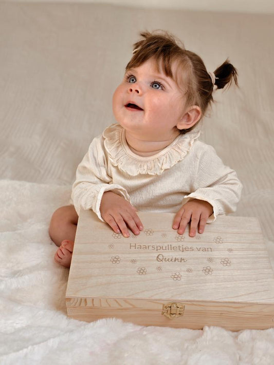 Een kindje heeft een gepersonaliseerde houten kist voor haarspulletjes vast met haar naam erop gegraveerd