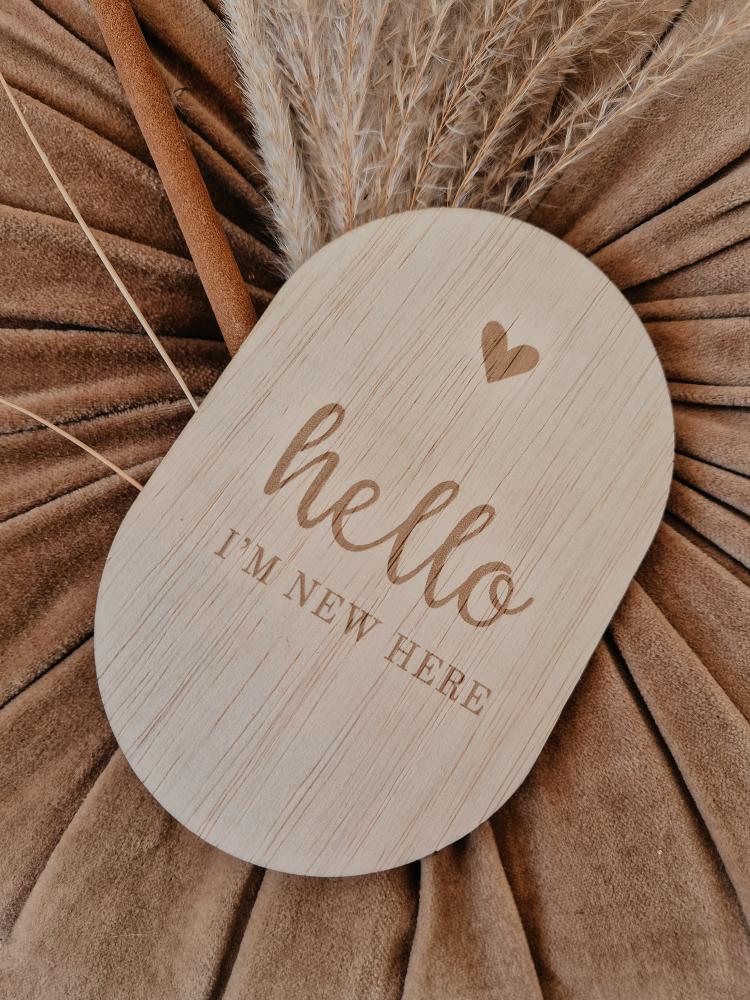 Een gepersonaliseerd ovaal houten bordje met tekst hello i'm new here