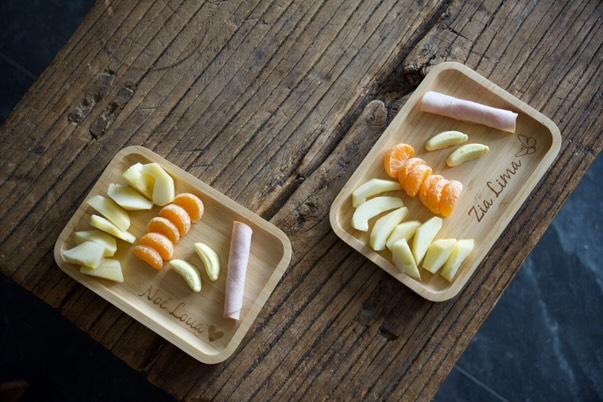 2 gepersonaliseerde broodplankjes staan op een tafel met fruit erop. de 1 is gepersonaliseerd met naam en een vlinder de ander met een naam en een hartje