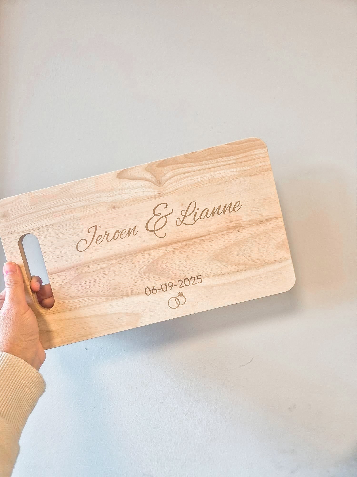 Gepersonaliseerde serveerplank met namen en trouwdatum en ringen erop. 