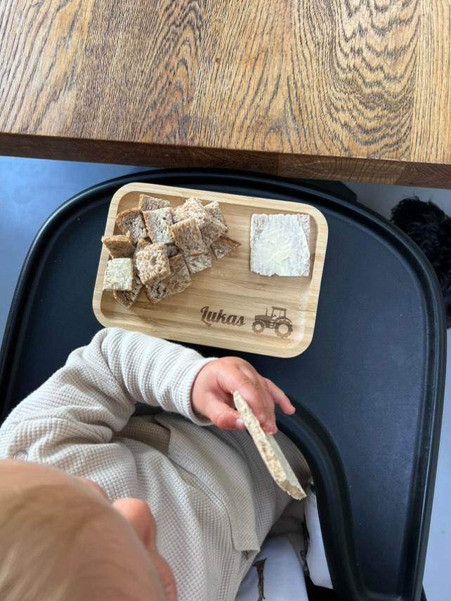 Een kindje heeft eten liggen op een gepersonaliseerd broodplankje met zijn naam erop en een trekker