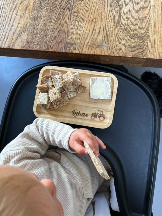 Een kindje heeft eten liggen op een gepersonaliseerd broodplankje met zijn naam erop en een trekker