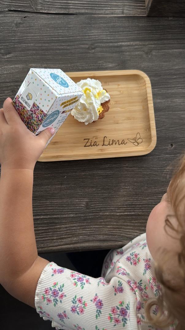 Meisje heeft een cupcake op een gepersonaliseerd broodplankje staan . Hierop staat haar naam gegraveerd met een vlinder ernaast
