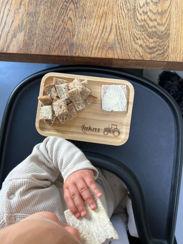 Een kindje heeft eten liggen op een gepersonaliseerd broodplankje met zijn naam erop en een trekker