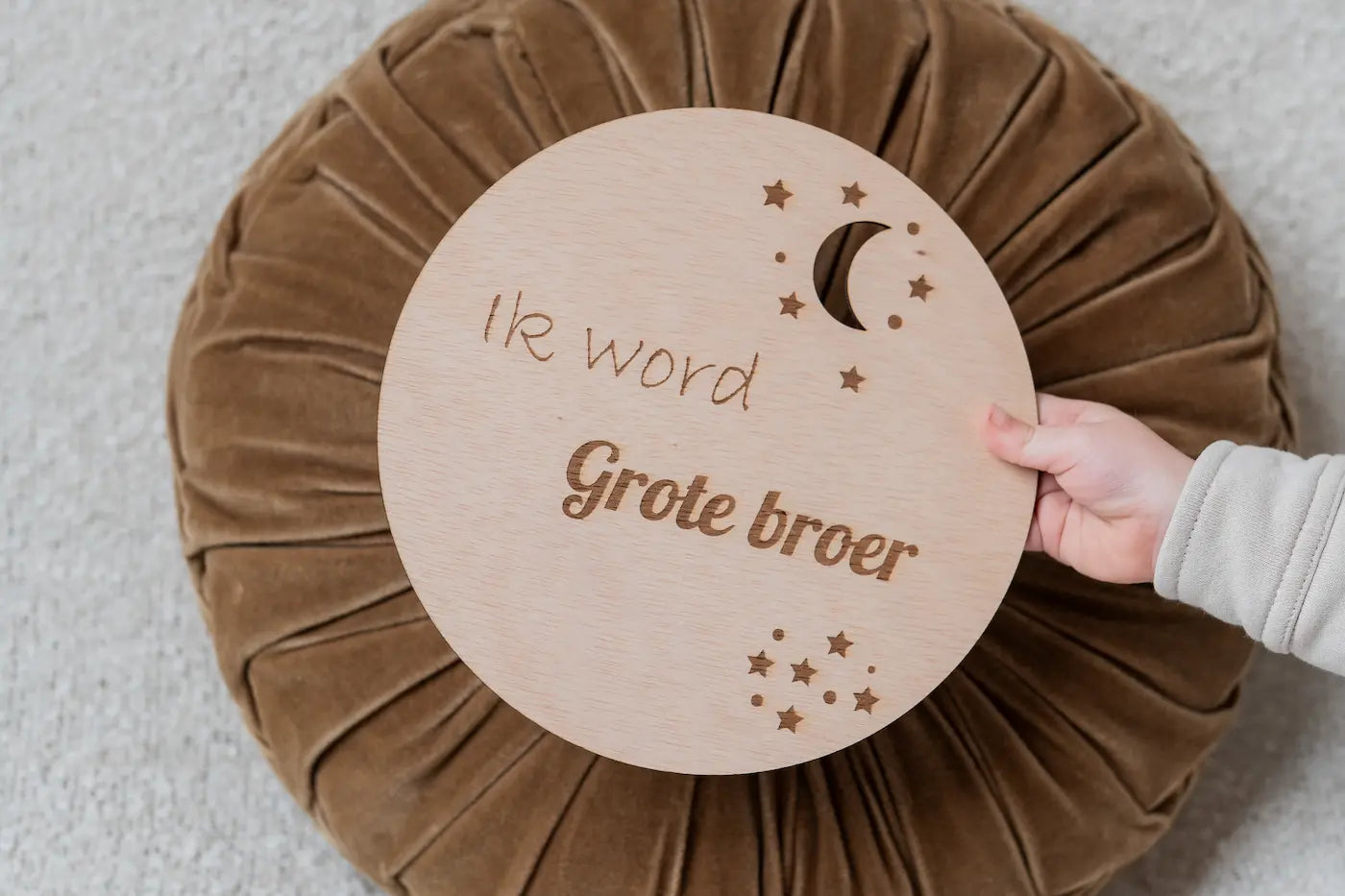 Kind houdt houten zwangerschapsaankondiging cirkel vast met tekst Ik word grote broer of zus tijdens zwangerschap aankondiging