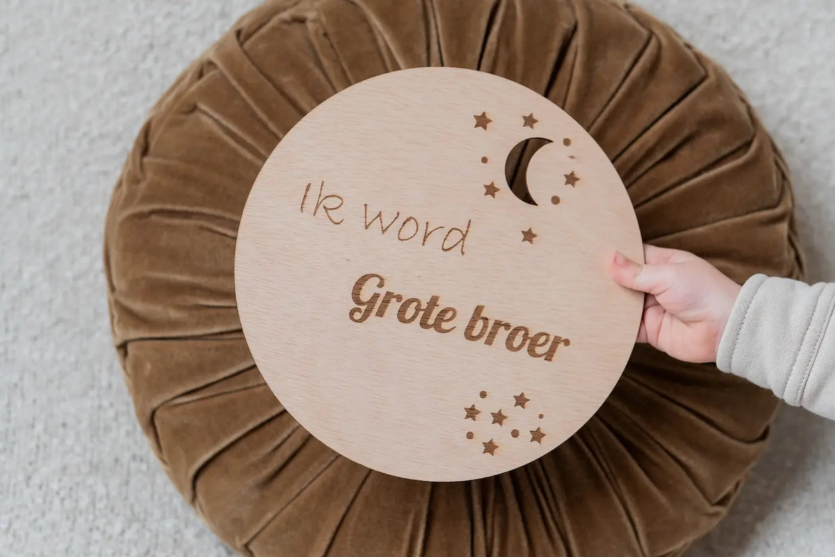 Kind houdt houten zwangerschapsaankondiging cirkel vast met tekst Ik word grote broer of zus tijdens zwangerschap aankondiging