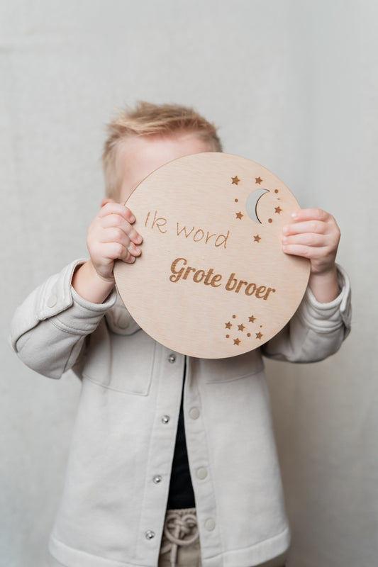 een kindje heeft een houten cirkel vast met daarop gegraveerd ik wordt grote broer