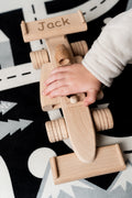 een kinderhandje dat een houten f1 auto vasthoudt met daarop een naam gegraveerd