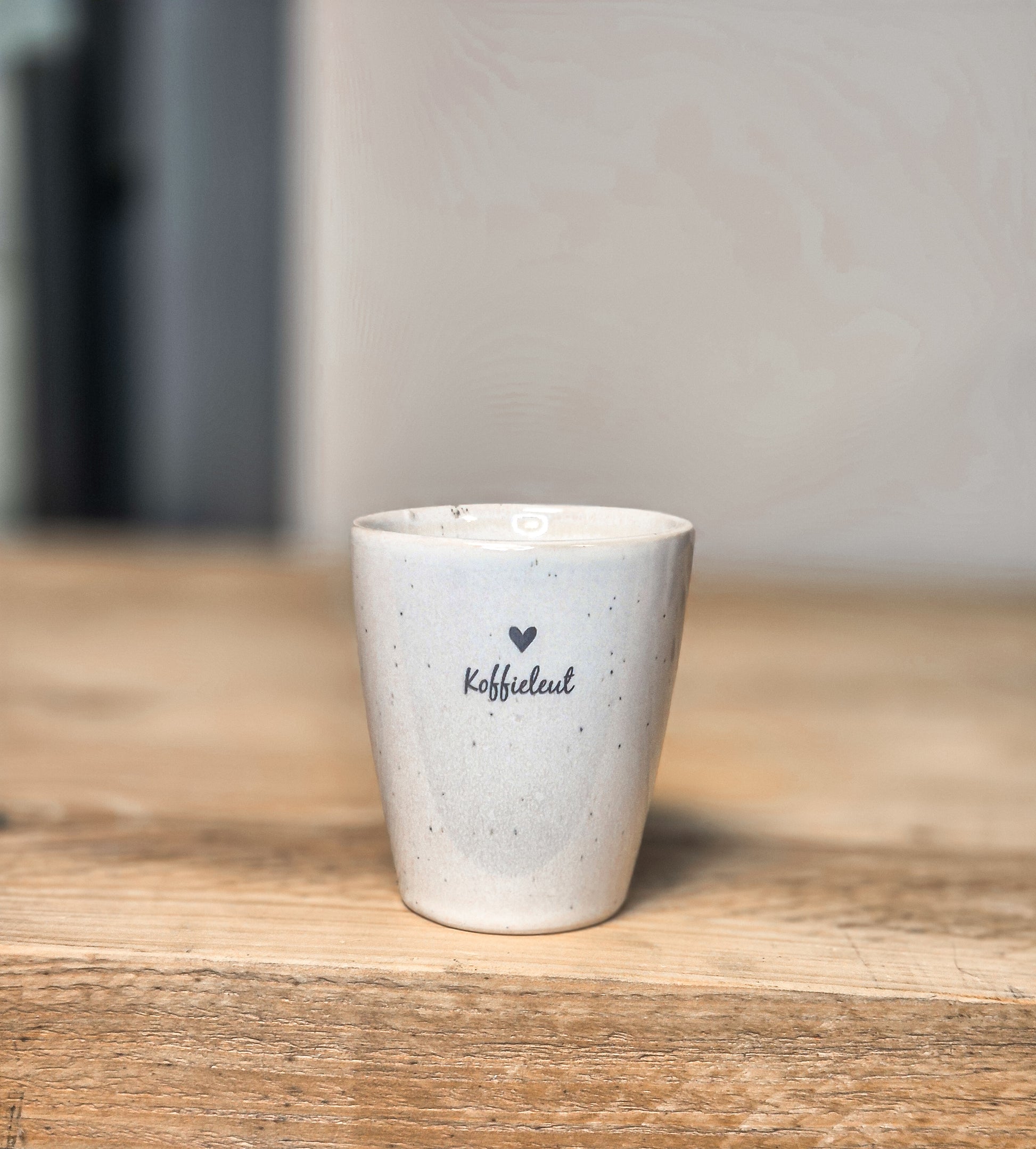 een witte mok met tekst koffieleut en een hartje